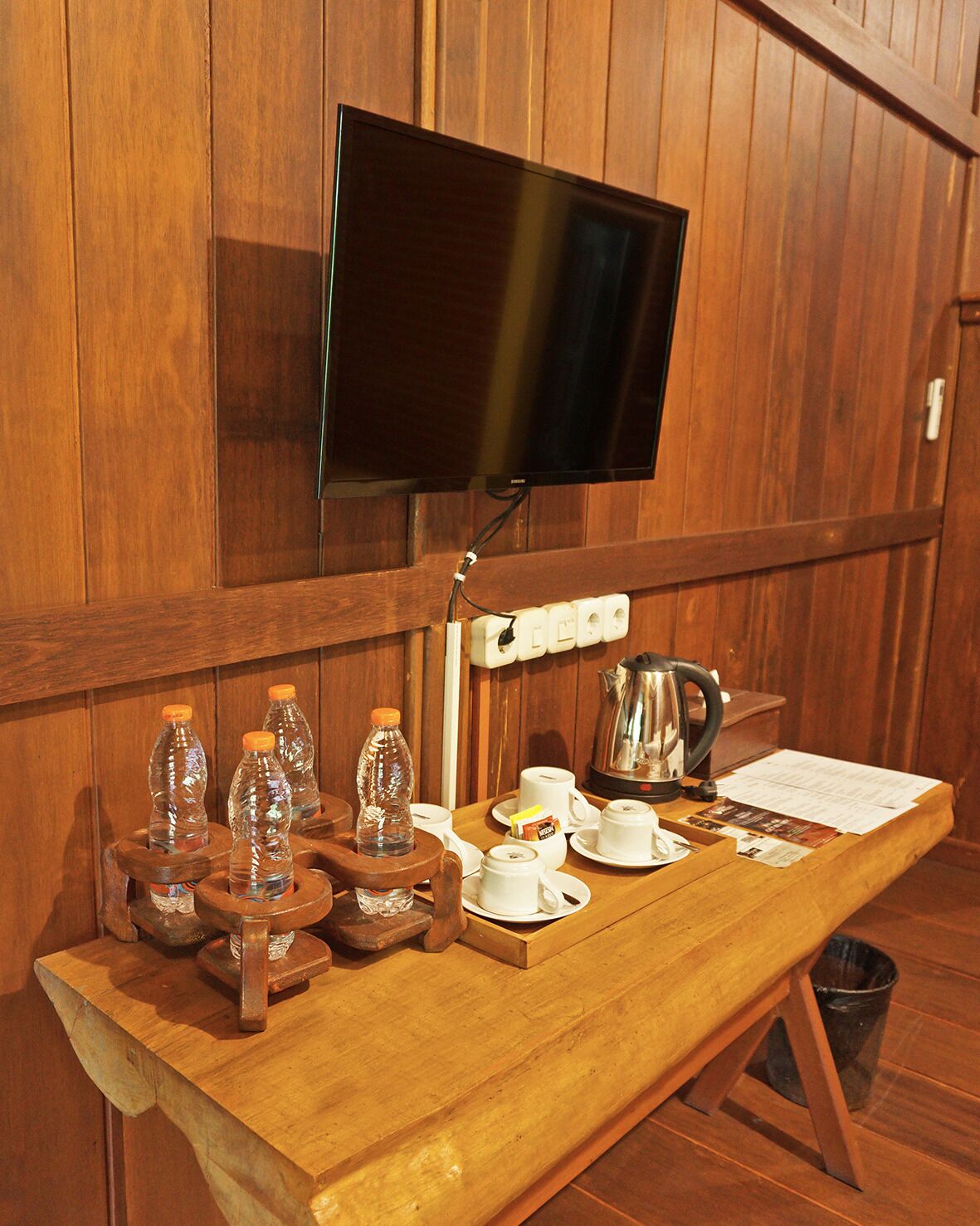 Eine Holztresorecke mit Wandfernseher, Wasserkocher, Tassen und Flaschen.