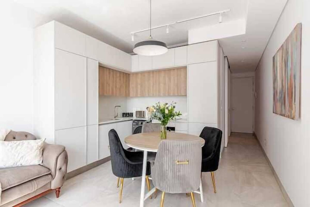 A modern kitchen with white cabinets, a wooden countertop, and a dining area with a round table and chairs.