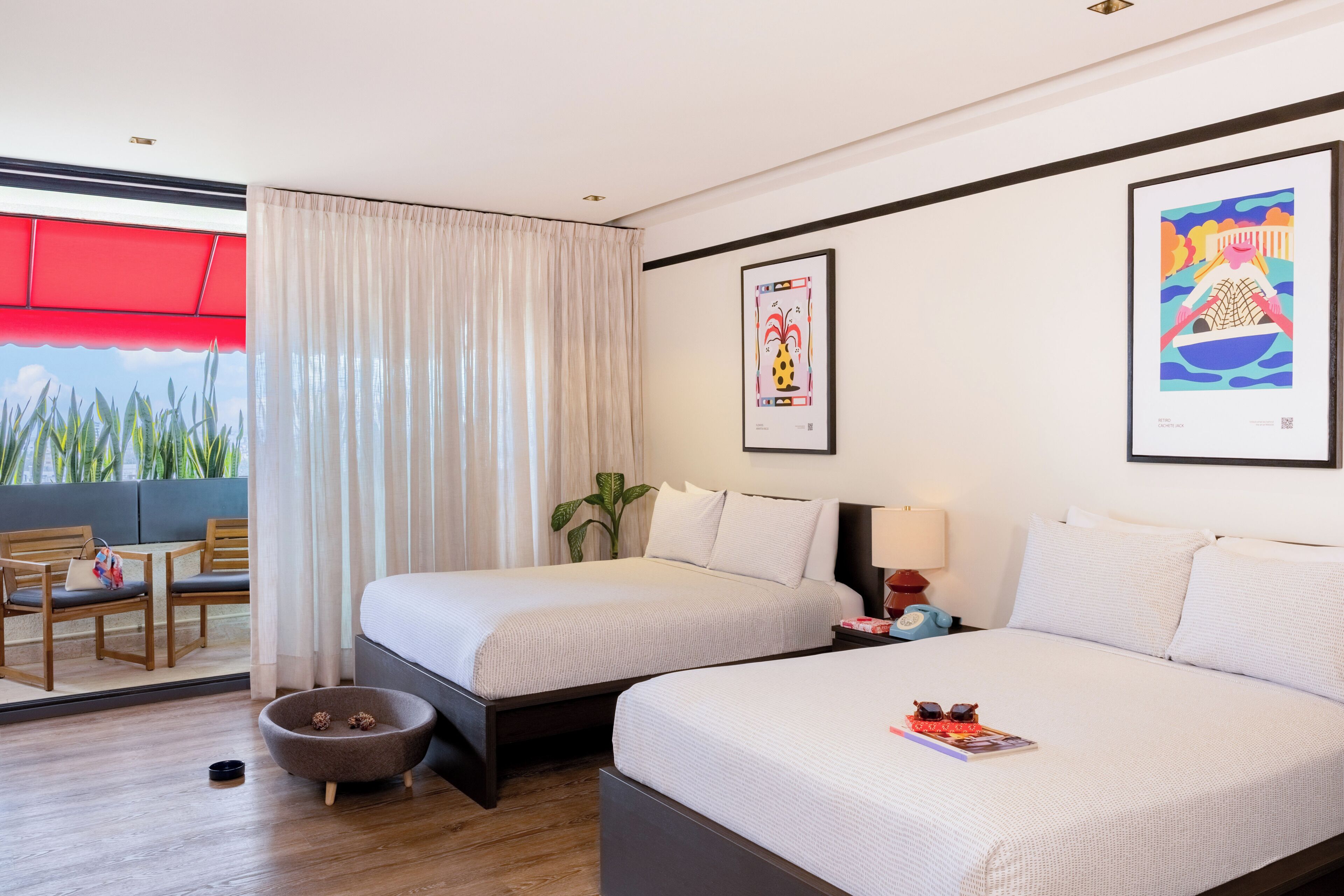 Une chambre d’hôtel avec deux lits, un coin repas comprenant des chaises et une table, et une vue sur la verdure environnante.