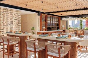 Un comedor con mesas redondas y sillas de mimbre, techo de madera y vista a la ciudad.