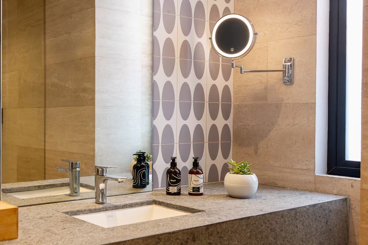 Un baño moderno con tocador, espejo, toallero y planta en maceta.