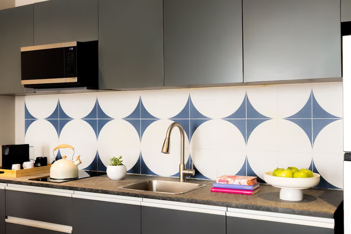 Una cocina moderna con armarios grises, un lavamanos de acero inoxidable, un microondas y un salpicadero decorativo.