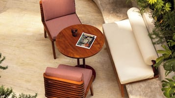 Un área de estar al aire libre iluminada por el sol, con una mesa redonda, dos sillones cómodos y un sofá.