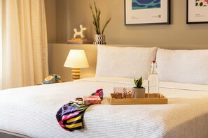 Una cama bien tendida con una bandeja de objetos, una lámpara y cuadros en la pared.