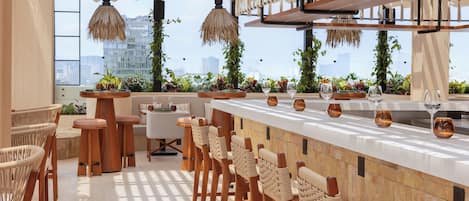 A modern bar area with high stools, a long counter, and hanging lights.