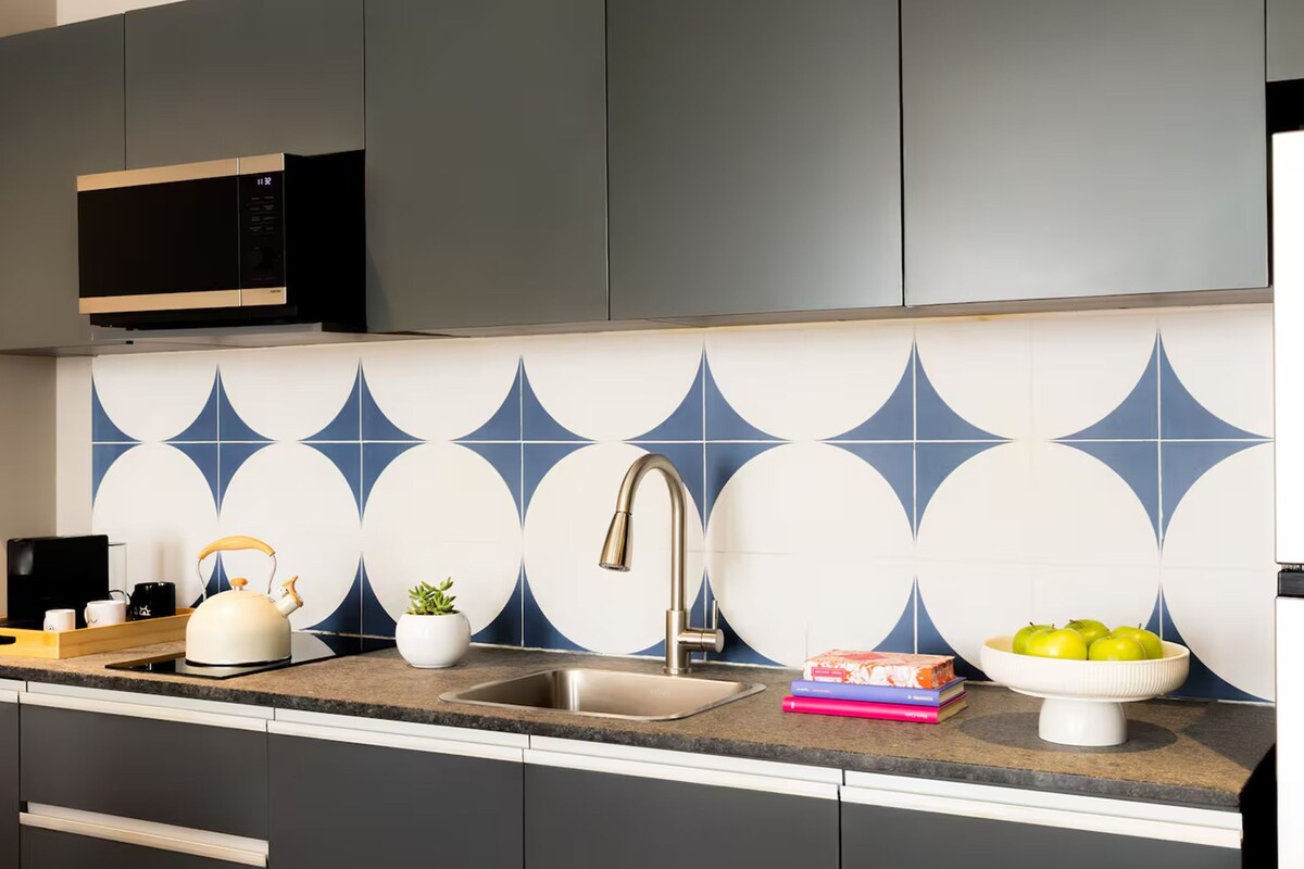 Una cocina moderna con armarios grises, un lavamanos de acero inoxidable, un microondas y un salpicadero decorativo.