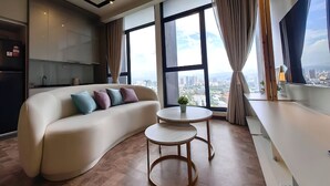A modern living room with a curved sofa, two small round tables, and large windows offering a city view.