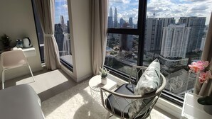 A modern room with a large window offering a city view, a comfortable chair, a small table, and a potted plant.