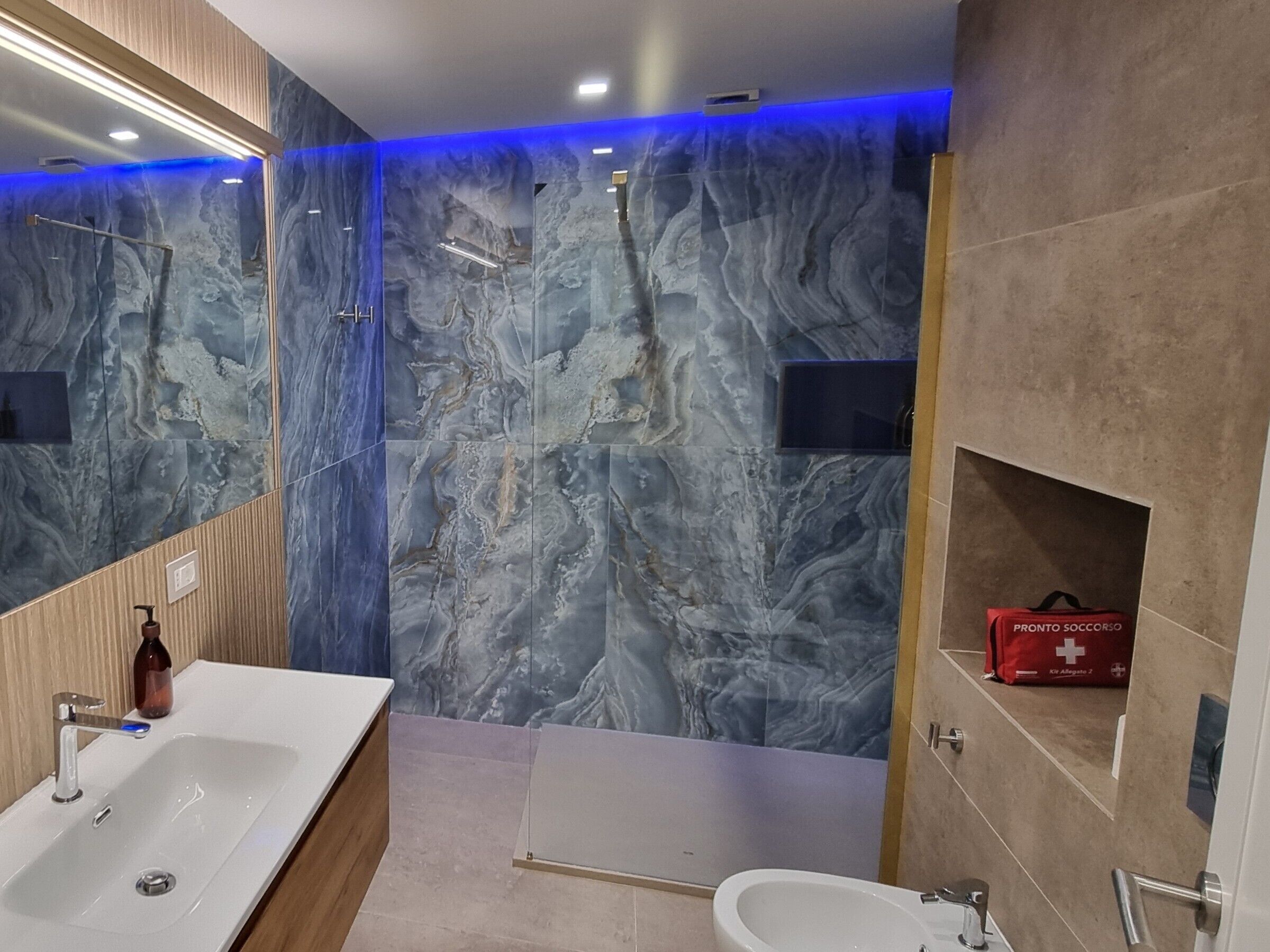 Un bagno moderno con rivestimento in marmo, uno specchio grande, una vasca da bagno, un lavandino e un bidet.