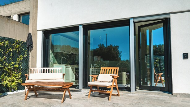 A patio with two wooden chairs and a table, a glass door entrance, and a concrete wall. - Il Piccolo Paradiso (Civitavecchia)