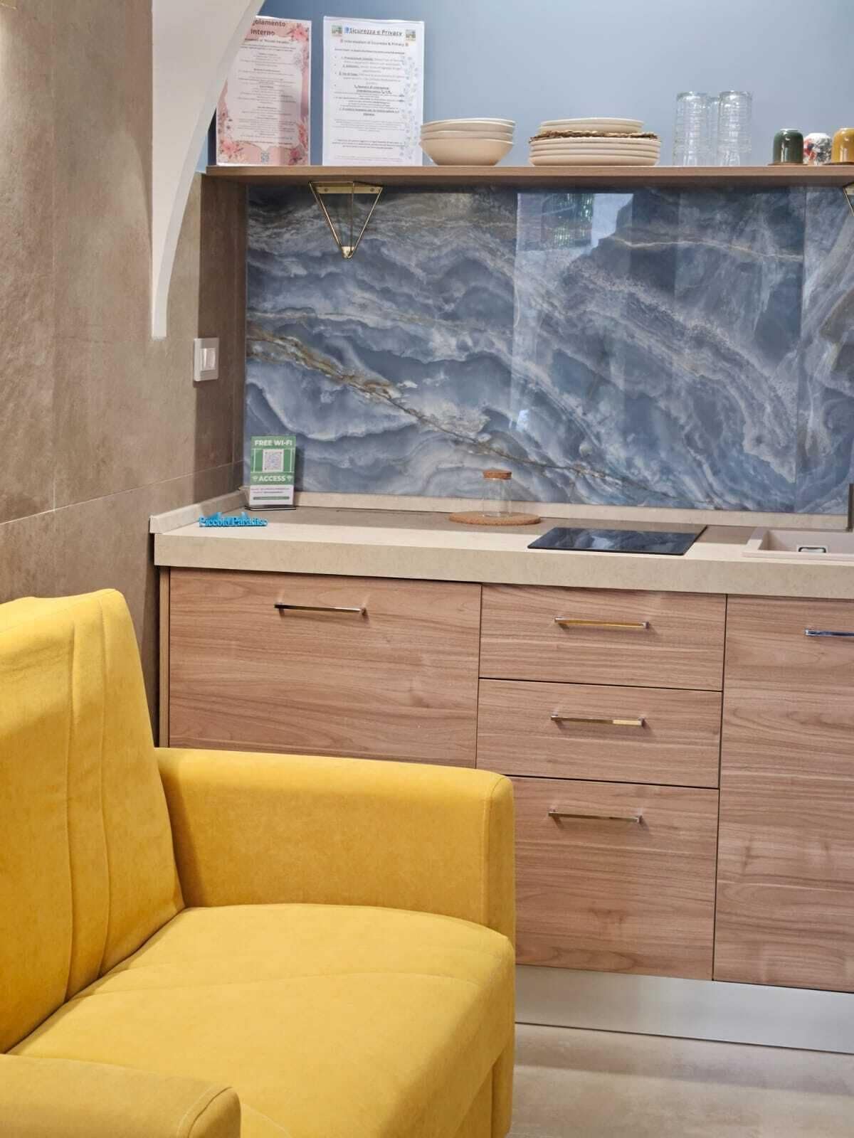 Una cocina moderna con protector mural de mármol, armarios de madera y un sillón amarillo.