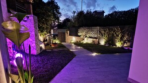 A well-lit outdoor patio area with a stone pathway, potted plants, and a stone wall. - Il Piccolo Paradiso (Civitavecchia)