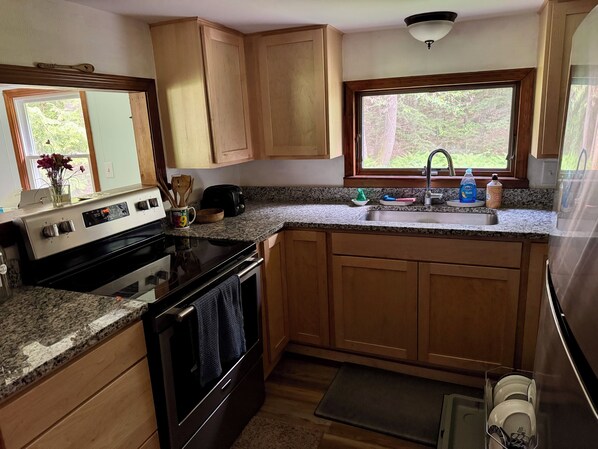 A kitchen with wooden cabinets, a granite countertop, a stove, an oven, a sink, and a window with a view of greenery.
