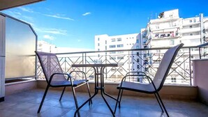 Ein Balkon mit zwei Stühlen und einem Tisch, der auf einen Stadtblick mit Gebäuden blickt.