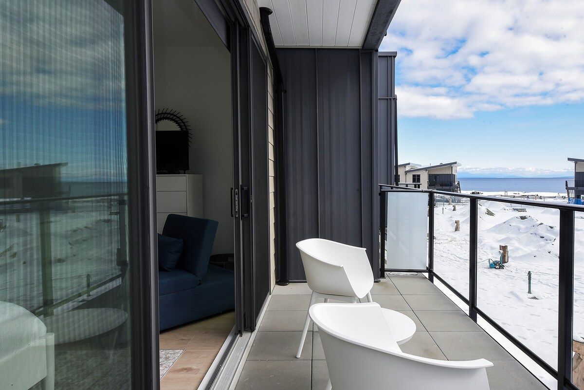 Ein Balkon mit Blick auf eine verschneite Landschaft, ein blaues Sofa und ein weißer Sessel.