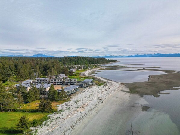 A coastal property with multiple buildings, a sandy beach, and a large body of water.