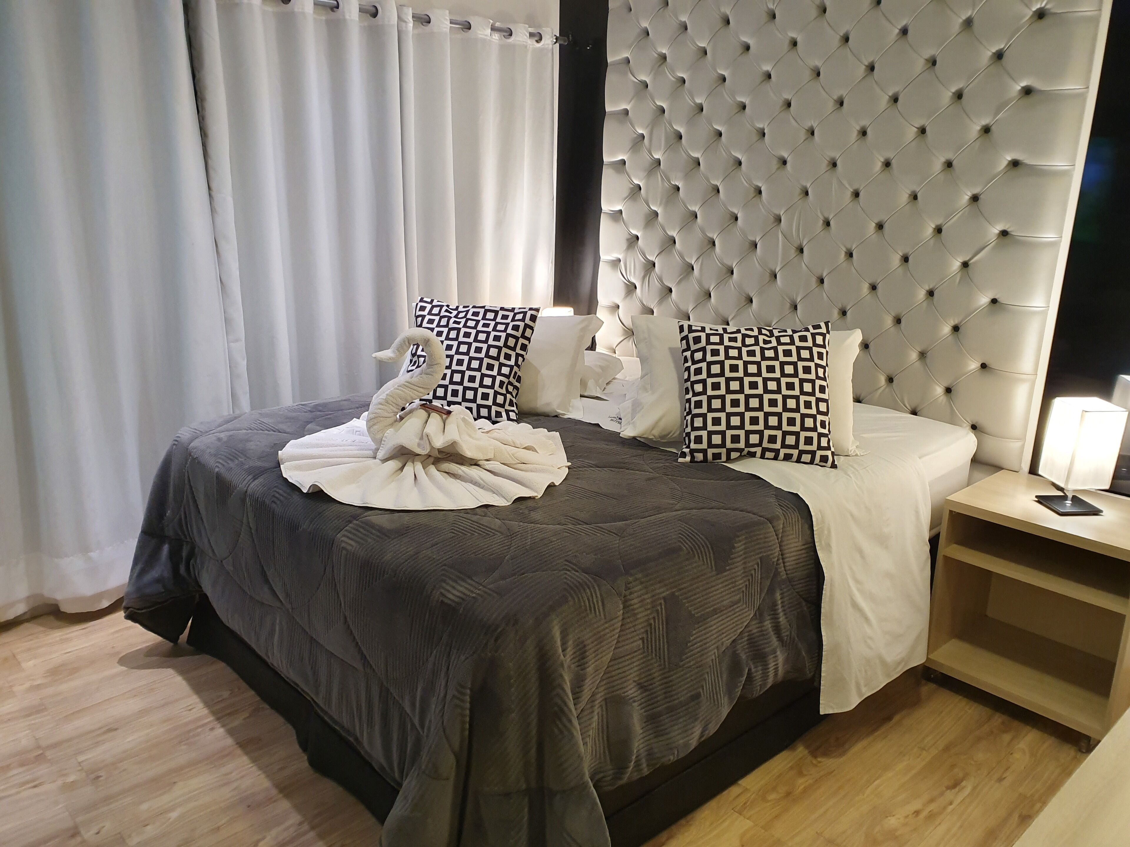Un letto rifatto con cura, con copripiumino grigio scuro, due cuscini decorati e un’elegante composizione di asciugamani a forma di cigno.