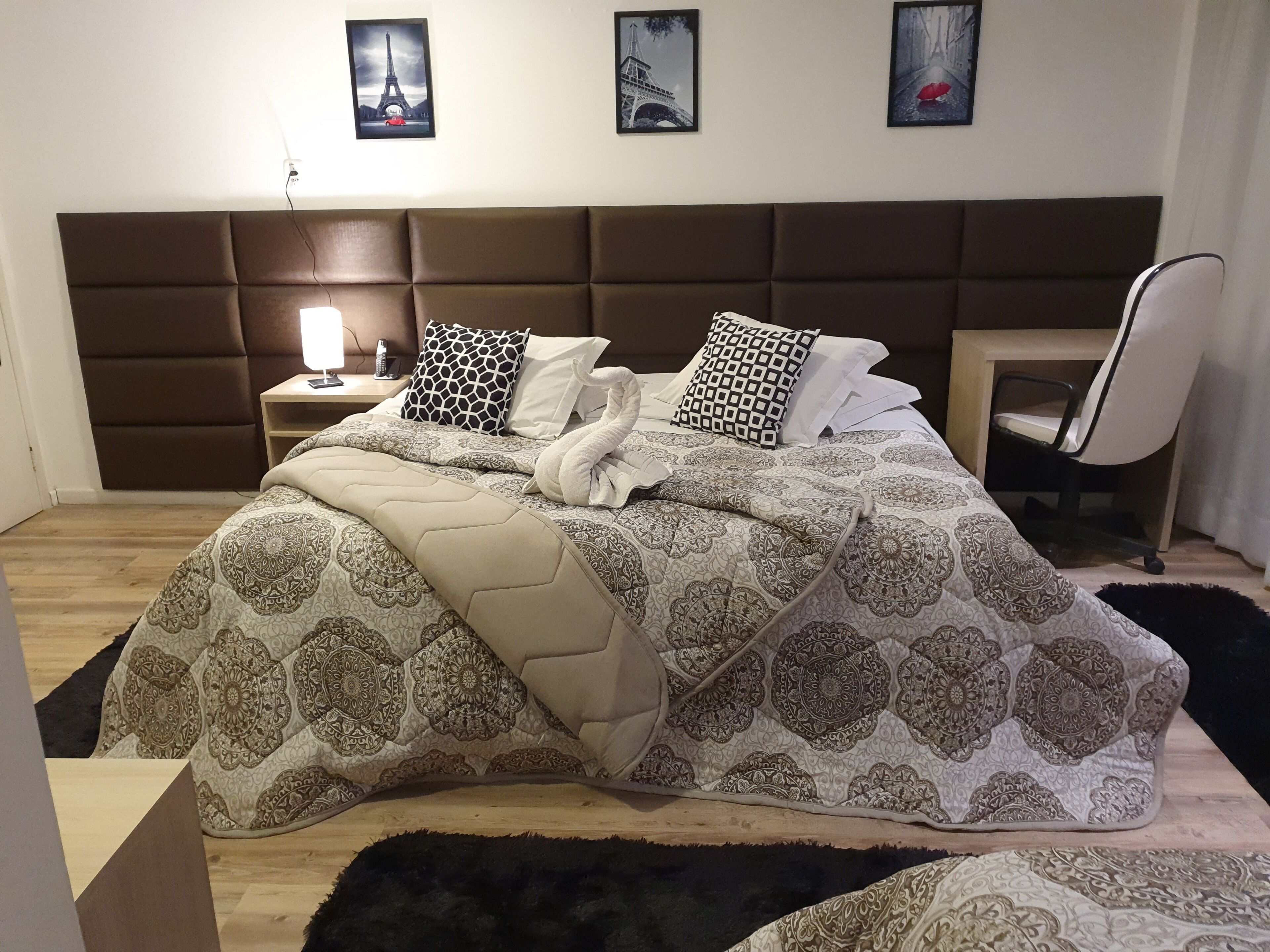 A neatly made bed with patterned bedding, a headboard, and a bedside table with a lamp.