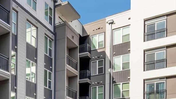 A modern apartment building with a swimming pool, sun loungers, and umbrellas.