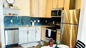 A modern kitchen with stainless steel appliances, wooden cabinets, and a dining area with two chairs and a table.