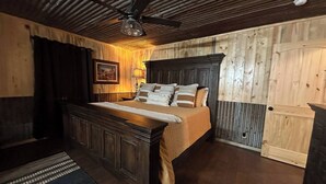 Ein Schlafzimmer mit Holzkopfteil, einem Bett mit vielen Kissen, einem Nachttisch, einer Lampe und einem Deckenventilator.