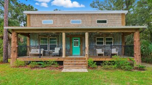 A two-story house with a porch, a green door, and a stone wall. - Sea Cow Retreat - Near Springs + Porch, Covered Deck & Fire Pit (Crystal River)