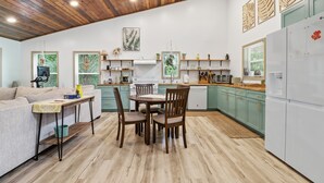 A modern kitchen with wooden ceiling, green cabinets, and a dining area with a table and chairs. - Sea Cow Retreat - Near Springs + Porch, Covered Deck & Fire Pit (Crystal River)