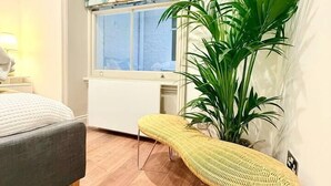 A bedroom with a bed, a bench, a potted plant, and a window with a view.