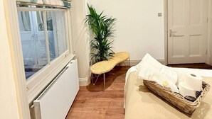 A bedroom with a large window, a potted plant, a bedside table with toiletries, and a door.