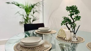 A modern dining area with a glass table, woven placemats, and a small bonsai tree centerpiece.