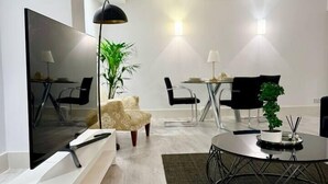 A modern living room with a flat-screen TV, a round dining table, two chairs, a sofa, a coffee table, and a potted plant.