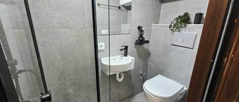 Un bany modern amb una dutxa de vidre, un lavabo blanc i un vàter.