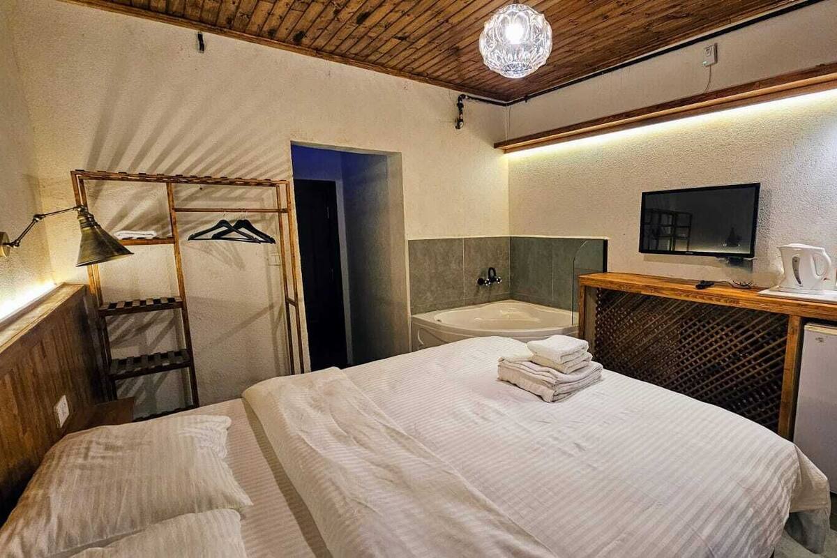 A hotel room with a bed, a desk with a computer, a small refrigerator, a mirror, and a shower area.