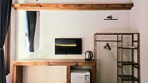 A compact room with a television mounted on the wall, a small wooden table with a kettle, and a metal shelf unit. - Mahzen Otel (Istanbul)