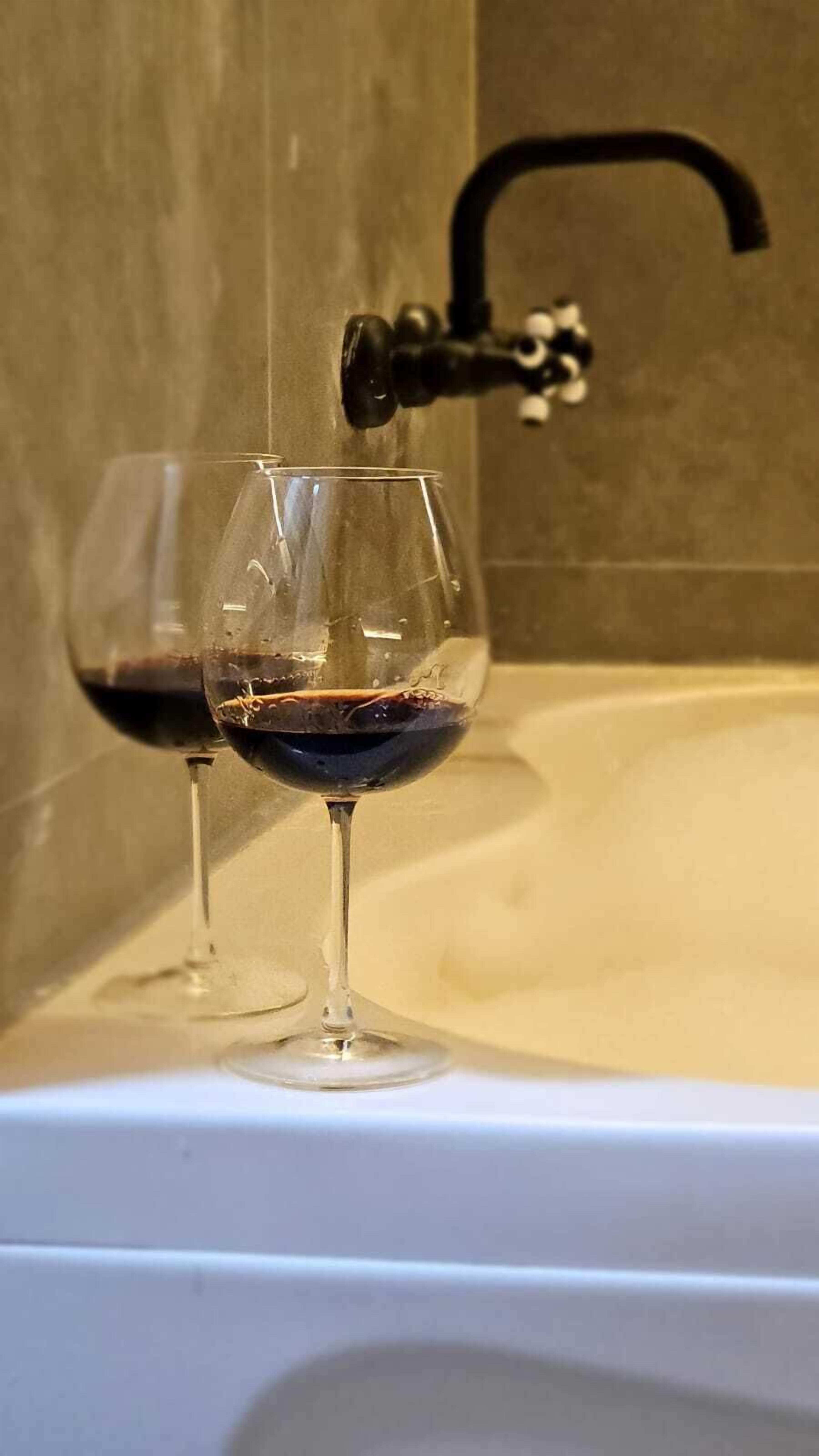 Deux verres à vin sont posés sur une surface blanche, avec un robinet visible à l’arrière-plan.