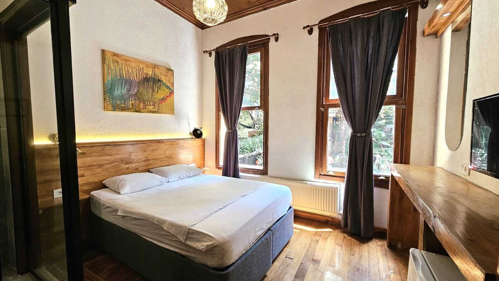 A bedroom with a bed, a desk, and a window with curtains.