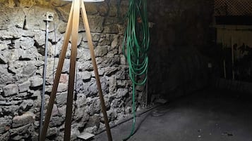 Una habitación con una pared de piedra, una lámpara amarilla sobre un trípode y una manguera de jardín verde.