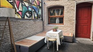 A small outdoor seating area with a table and bench, a red door, and a brick wall with a colorful mural. - Mahzen Otel (Istanbul)
