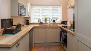 A compact kitchen with a built-in dishwasher, a sink, and a window with blinds. - Poddington Cottage (Salisbury)