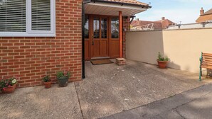 A brick house with a tiled roof, a wooden front door, and a small porch. There are potted plants and a bench outside. - Poddington Cottage (Salisbury)