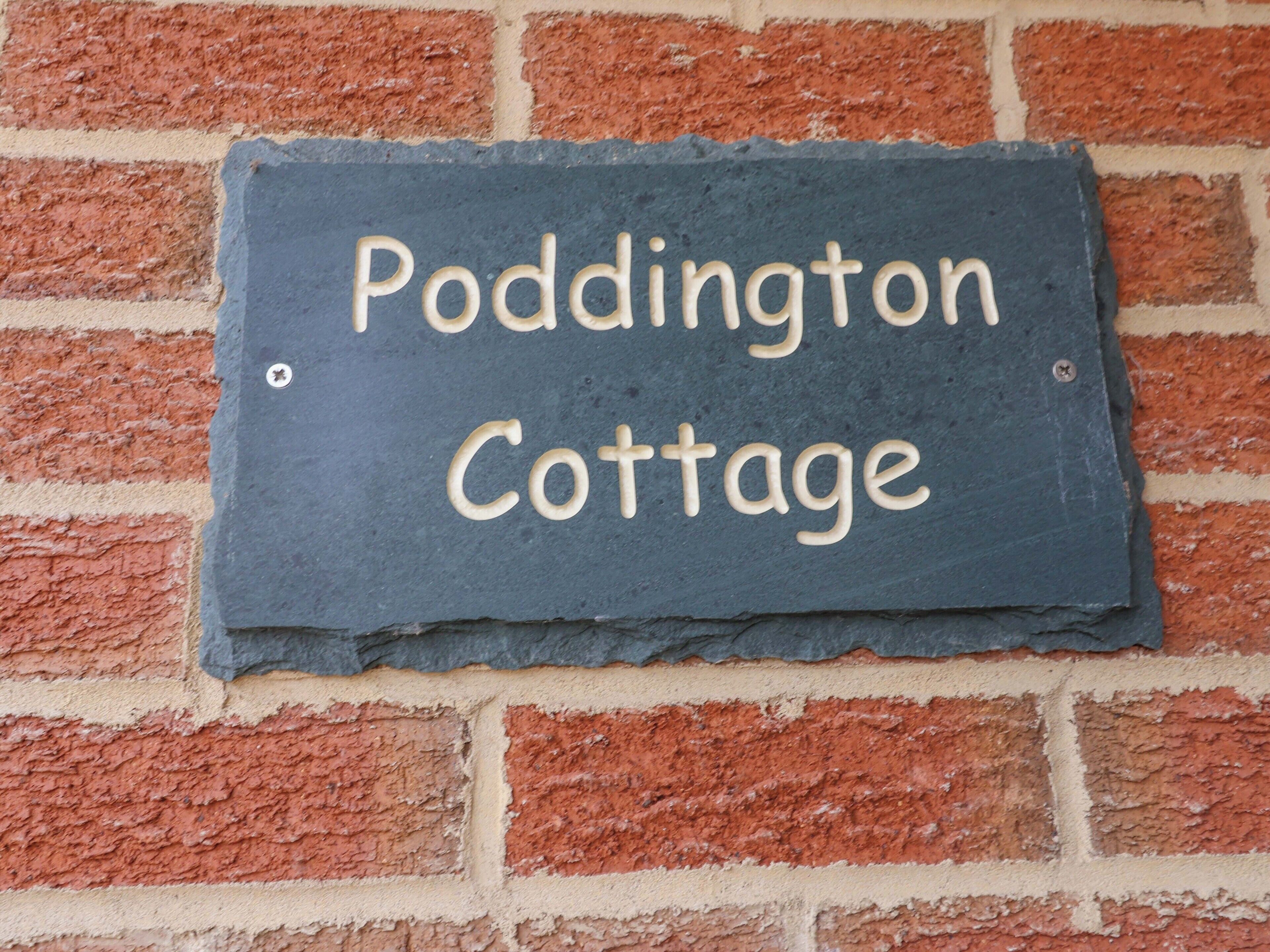 A slate sign with "Paddington Cottage" written on it, mounted on a brick wall.