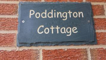 A slate sign with "Paddington Cottage" written on it, mounted on a brick wall.