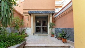 A building entrance with a tiled pathway leading to a glass door. There are potted plants on either side of the entrance. - Elegant apartment (Catania)