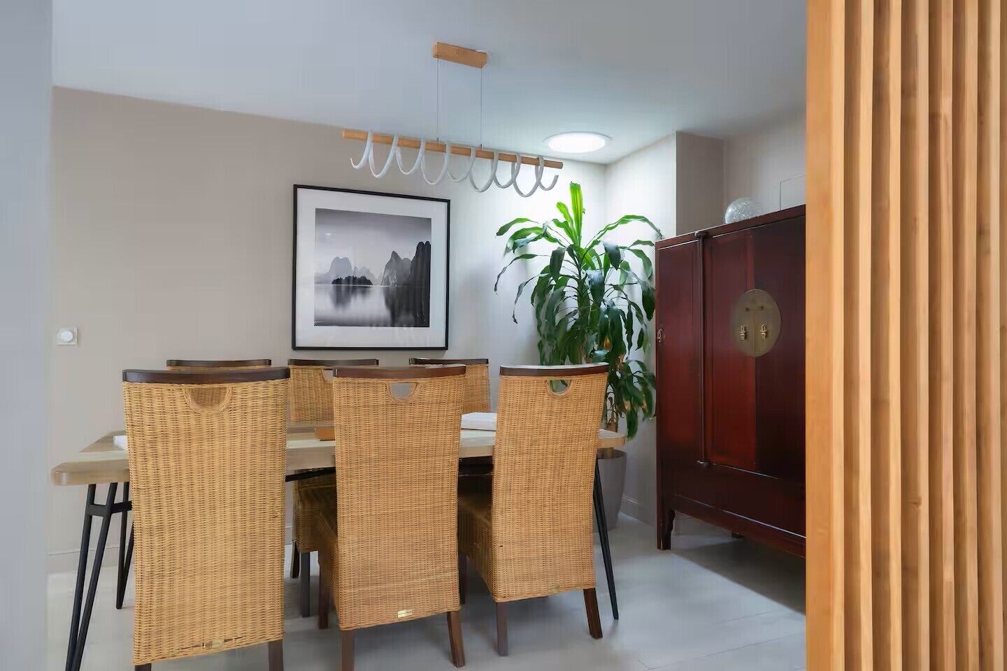 Een eetgedeelte met rieten stoelen, een tafel, een lijst met foto, een potplant en een houten kast.