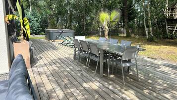 Um terraço ao ar livre com uma mesa de jantar e cadeiras, cercado por árvores e uma cerca de madeira.