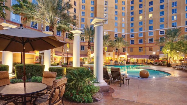 A hotel courtyard with a swimming pool, outdoor seating, palm trees, and a large building in the background. - Lovely Las Vegas 1BD Suite Near the Strip! (Las Vegas)