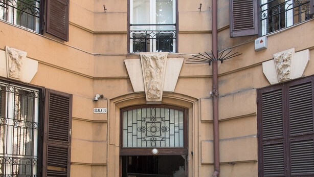 Ein Gebäudeeingang mit gefliestem Boden, einer Tür mit Fensterglas und zwei Blumentöpfen.