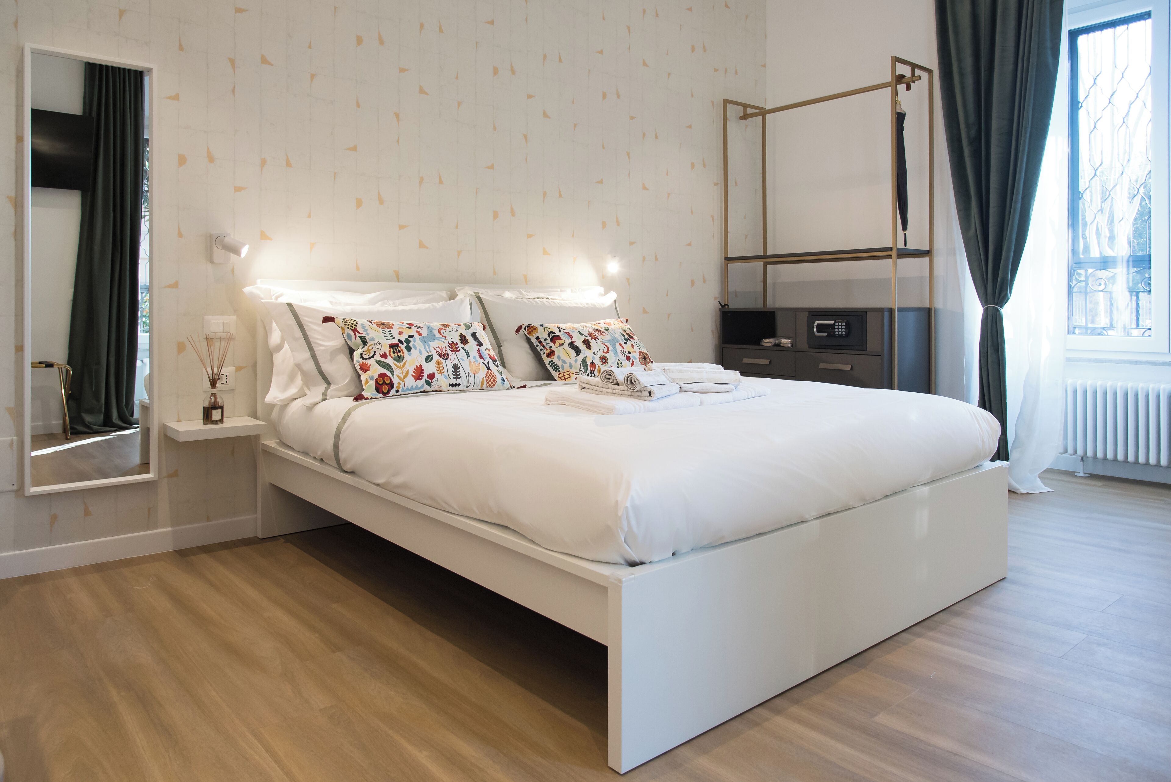 A modern bedroom with a large bed, bedside tables, a mirror, and a window with curtains.