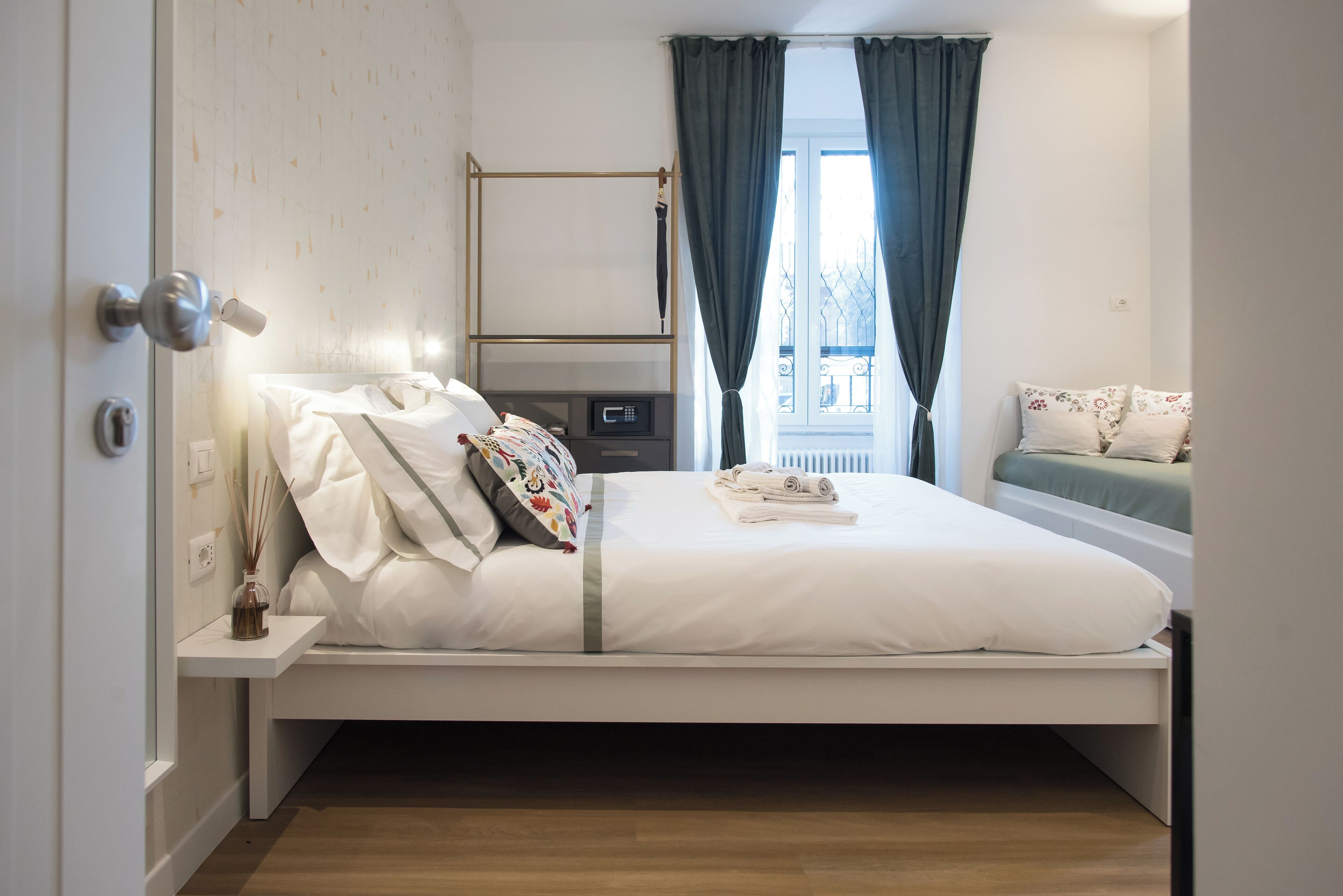 A neatly made bed with white linens, a bedside table with a lamp, and a window with curtains.