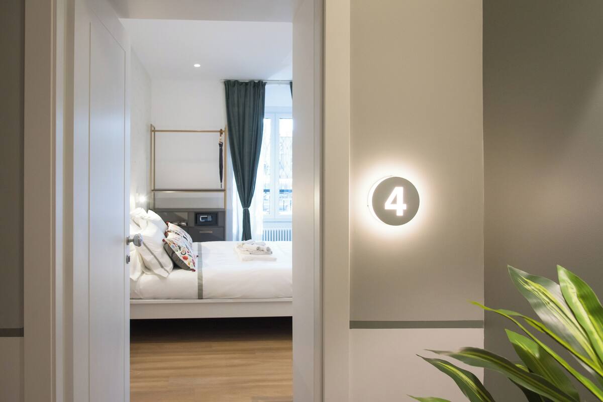 A hotel room with a bed, a bedside table, a lamp, and a window with curtains.